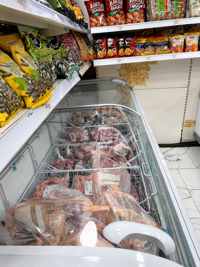 Chest freezer of frozen meat cuts beside shelves of roasted peanuts