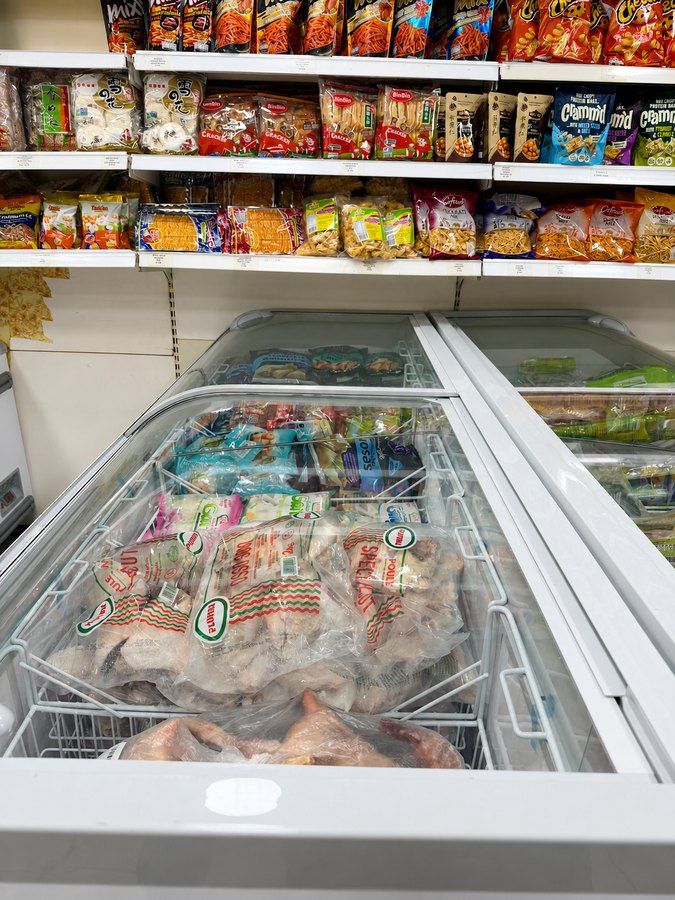 Chest freezer of frozen whole chicken and poultry portions under a rice cracker shelf